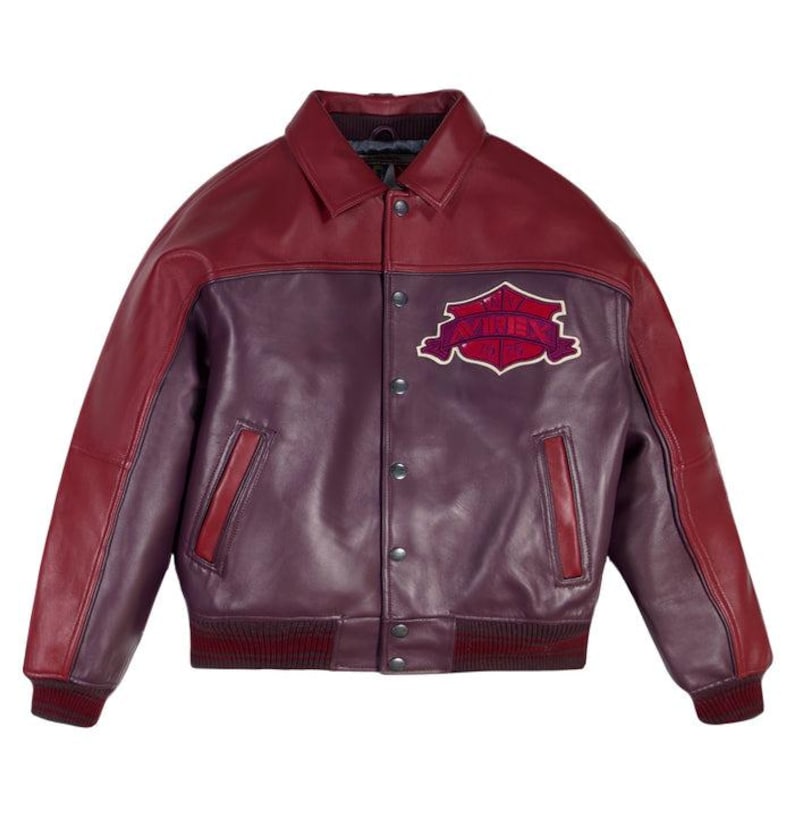 K&ouml;nnte beinhalten: Burgunderrote und violette Lederjacke mit Kragen und Knopfleiste. Die Jacke hat einen Aufn&auml;her auf der Brust mit dem Wort "AVIREX" in einer stilisierten Schriftart. Gerippte B&uuml;ndchen und Saum.
