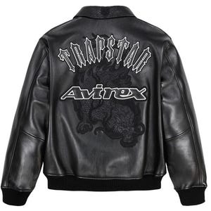 Könnte beinhalten: Schwarze Lederjacke mit geripptem Kragen und Bündchen. Auf dem Rücken befindet sich ein großes gesticktes Drachendesign mit den weißen Worten "TRAPSTAR" und "Avirex".