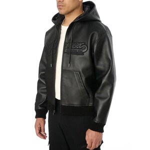 May include: Black leather hooded jacket with a zip-up front, featuring the word "Merx" embroidered on the chest. The jacket has a ribbed hem and cuffs, and a drawstring hood. The model is wearing a white t-shirt underneath.