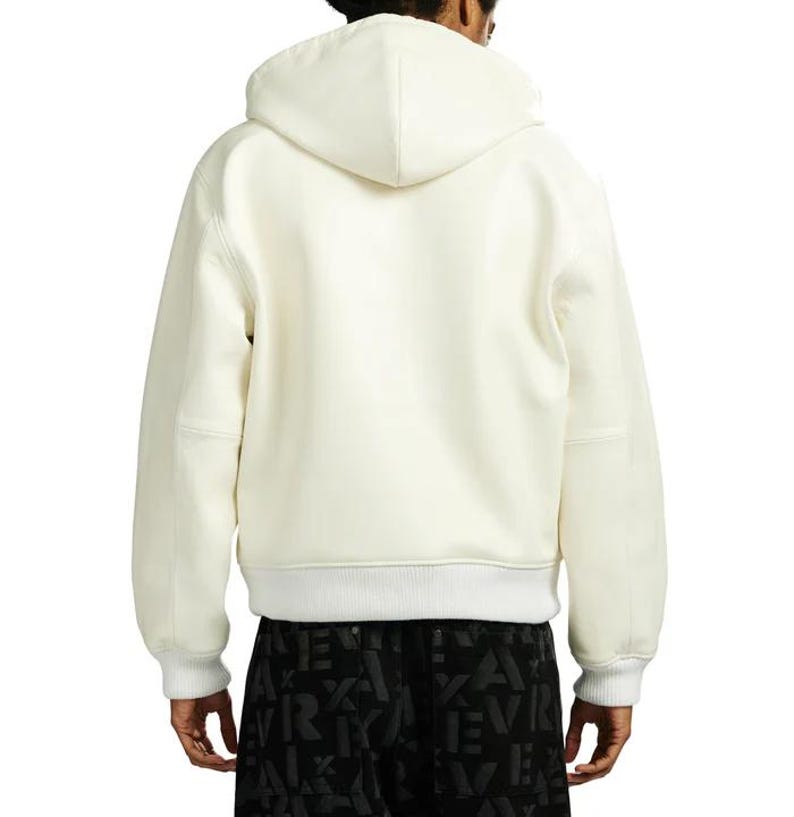 May include: Cream-colored hooded sweatshirt with a white ribbed hem and cuffs. The back view shows a minimalist design with a hood and long sleeves. The sweatshirt is made of a soft, comfortable material.