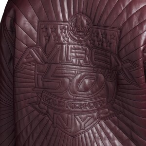May include: A burgundy leather jacket with quilted stitching. The back of the jacket features an embroidered design with the text "AVIREX 50 GOLD KICK-OFF NY" and star and crown details.
