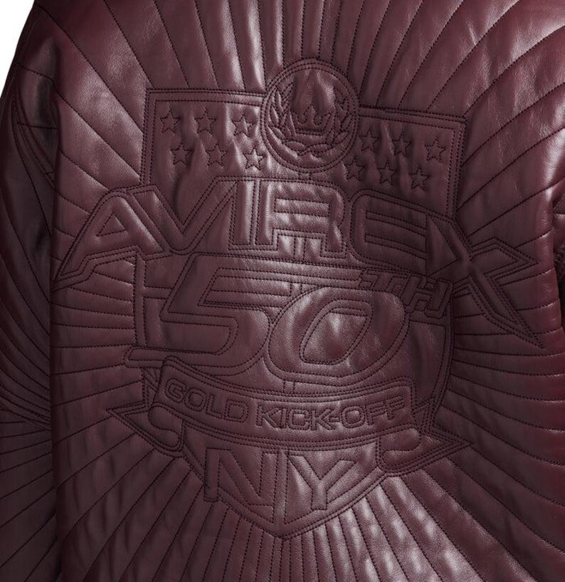 May include: A burgundy leather jacket with quilted stitching. The back of the jacket features an embroidered design with the text "AVIREX 50 GOLD KICK-OFF NY" and star and crown details.