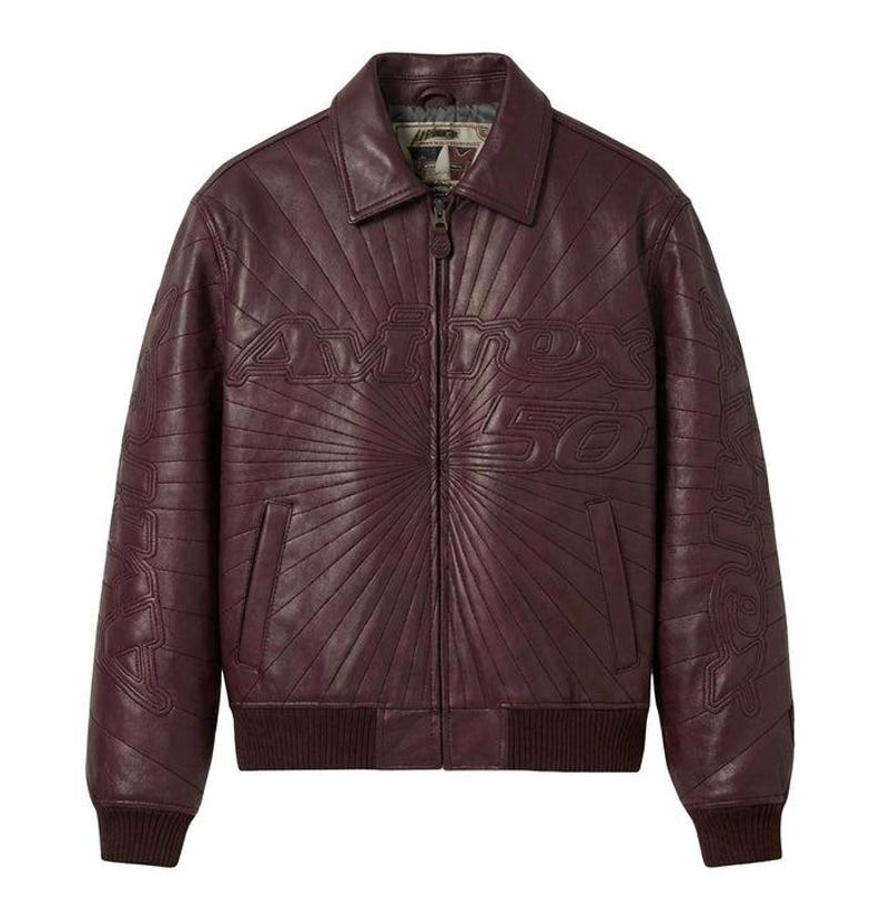 May include: A burgundy leather jacket with a ribbed collar, cuffs, and hem. The jacket features a zip-up front and the text "Avirex 50" embossed on the chest. The design includes a sunburst pattern radiating from the text.