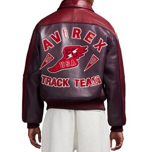 K&ouml;nnte beinhalten: Burgunderrote und dunkelviolette Lederjacke mit dem Text "AVIREX TRACK TEAM" auf dem R&uuml;cken. Die Jacke hat ein rot-wei&szlig;es Logo mit einem gefl&uuml;gelten Schuh und dem Text "USA". Sie hat einen gerippten Saum und B&uuml;ndchen.