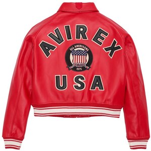 May include: A red leather jacket with the word "AVIREX" across the back in black letters with white trim. Below the word "AVIREX" is a patch with the words "ALL AMERICANS" and "ESTABLISHED 1975". The word "USA" is below the patch.