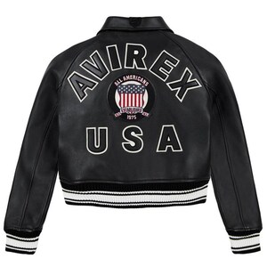 Puede incluir: Chaqueta de cuero negra con letras blancas "AVIREX" y "USA". Un parche circular con la bandera estadounidense est&aacute; centrado en la espalda. La chaqueta tiene cuello, pu&ntilde;os y dobladillo acanalados con rayas blancas.