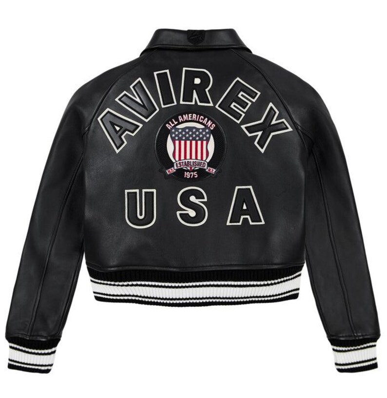 Puede incluir: Chaqueta de cuero negra con letras blancas "AVIREX" y "USA". Un parche circular con la bandera estadounidense est&aacute; centrado en la espalda. La chaqueta tiene cuello, pu&ntilde;os y dobladillo acanalados con rayas blancas.