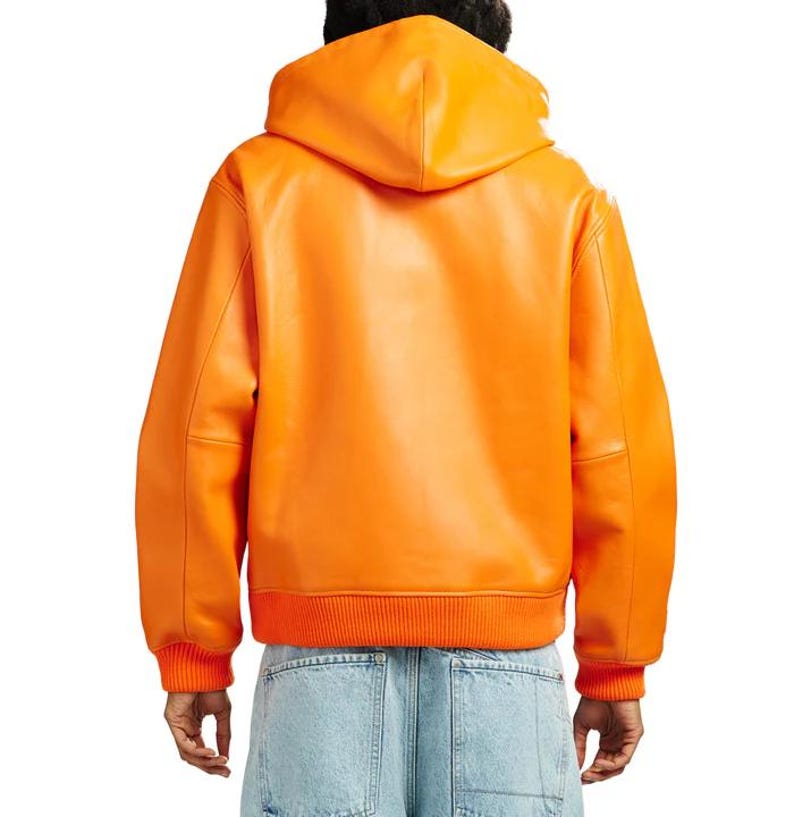 May include: Bright orange leather hooded jacket with ribbed cuffs and hem. The jacket features a classic bomber style with a hood and a smooth, glossy finish. The back view showcases the jacket's clean lines and vibrant color.