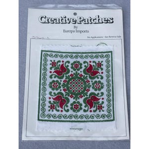 May include: A square fabric patch with a detailed floral design in red and green. The patch is bordered with green swirls and features the text "Creative Patches by Europa Imports."
