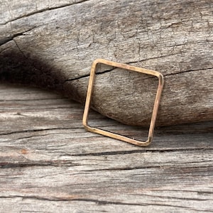 May include: A gold-toned square ring with a hammered finish. The ring is made of metal and has a simple, geometric design.