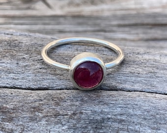Puede incluir: Un anillo de plata con una piedra preciosa redonda de color rosa oscuro, tallada en cabujón.