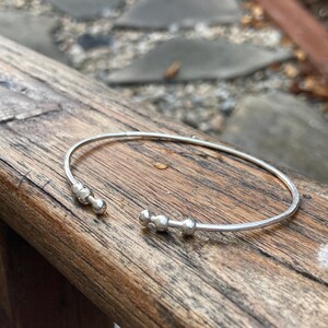 May include: A silver bangle bracelet with three small round beads on one side.