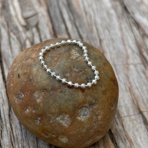 May include: A silver chain ring with a beaded design. The ring is on a brown rock.