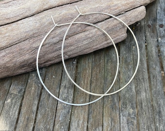 May include: A pair of silver hoop earrings. The hoops are large and round, and they are made of a thin, delicate wire.