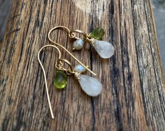 May include: Gold earrings with a teardrop-shaped moonstone, a small pearl, and a green gemstone.