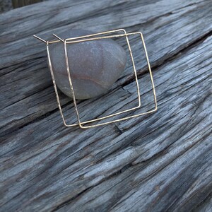 May include: A pair of gold square hoop earrings. The earrings are made of hammered wire and have a simple, modern design.
