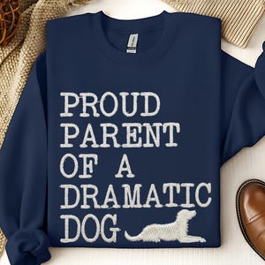 May include: Navy blue sweatshirt with the text "PROUD PARENT OF A DRAMATIC DOG" in white, along with a white dog illustration. The sweatshirt is a casual garment, perfect for dog lovers.
