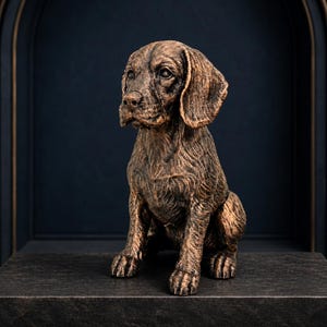 Könnte beinhalten: Eine bronzefarbene Hundefigur in sitzender Position. Die Skulptur zeichnet sich durch eine detaillierte Fellstruktur, Schlappohren und einen realistischen Gesichtsausdruck mit dunklen Augen aus. Das Finish hat einen metallischen Glanz.