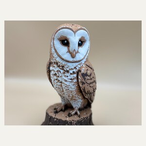 Può includere: Una statuetta di barbagianni con un disco facciale bianco a forma di cuore, occhi scuri e un piumaggio maculato marrone e bianco. Il gufo è appollaiato su una base a forma di tronco d'albero marrone testurizzato, con dettagli piumati.
