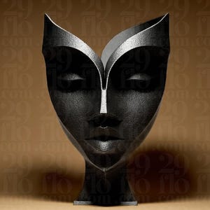 Könnte beinhalten: Eine schwarze dekorative Gesichtsskulptur mit geschlossenen Augen und einer weißen Linie auf der Nase. Die Skulptur hat eine strukturierte Oberfläche und steht vor einem braunen Hintergrund. Die Skulptur ist etwa 30 cm hoch.