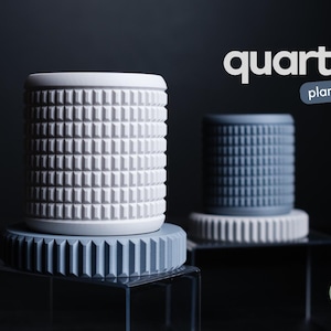 May include: Two cylindrical quartz planters, one white and one grey-blue, with a textured, geometric pattern. The planters sit on matching circular bases. The word "quartz" and "planter" are displayed in white text.