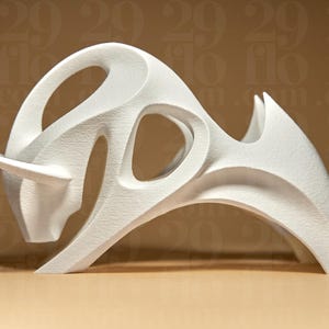 Könnte beinhalten: Eine weiße, abstrakte Skulptur eines Bullen mit strukturierter Oberfläche. Die Skulptur hat eine geschwungene Form mit offenen Räumen und einem einzelnen Horn. Das Kunstwerk wird auf einer hellbraunen Oberfläche präsentiert.