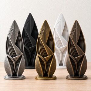 May include: Five vertical sculptures with pointed tops and layered, geometric leaf-like patterns. The set includes one silver, one matte black, one antique gold, one white, and one bronze finish, each standing on a circular base.