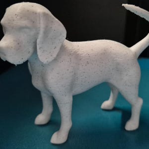 Puede incluir: Una figura de perro de color blanco con pequeñas motas negras por todo el cuerpo. El perro está de pie en posición de perfil con la cabeza ligeramente girada hacia la izquierda, con orejas caídas y una cola que se curva hacia arriba.