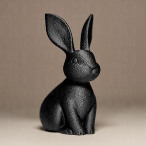 Può includere: Una statuetta di coniglio nero con dettagli strutturati. Il coniglio è in posizione seduta con le orecchie dritte. La scultura è di colore nero pieno ed è ambientata su uno sfondo neutro.