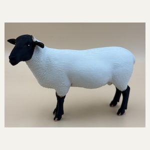 Könnte beinhalten: Eine Schaf-Figur mit einem einfarbig schwarzen Kopf und vier schwarzen Beinen, die sich von einem strukturierten weißen Körper abheben. Das Tier ist in stehender Position dargestellt und zeigt eine glatte, matte Oberfläche am Kopf sowie eine detaillierte, geriffelte Oberflächenstruktur am weißen, wolligen Rumpf.
