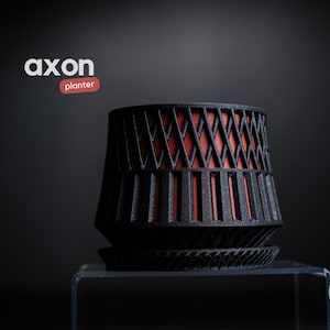 Könnte beinhalten: Schwarzer und roter Pflanztopf mit geometrischem Design. Der Pflanztopf hat eine zylindrische Form mit einem gitterartigen Äußeren und einem roten Innenraum. Die Wörter "axon" und "planter" befinden sich in der oberen linken Ecke.