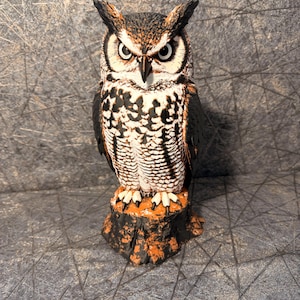 May include: A detailed owl figurine featuring black, white, and brown plumage with prominent ear tufts and sharp talons. The owl is perched on a textured, orange and black tree stump base, displaying intricate feather patterns and a focused gaze.