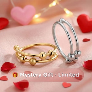 May include: Two rings, one gold and one silver, are displayed on a pink surface with heart-shaped decorations. The gold ring has two bands with small gold beads. The silver ring has two bands with silver beads. Text reads "Mystery Gift - Limited".