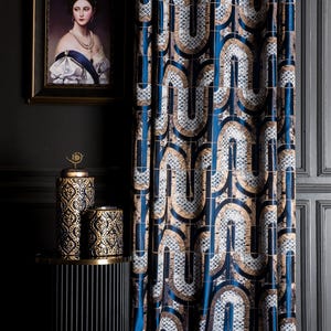 May include: A luxurious curtain with a repeating geometric pattern in shades of blue, gold, and white. The curtain hangs next to a framed portrait and decorative black and gold jars on a small table. The overall theme is home decor.