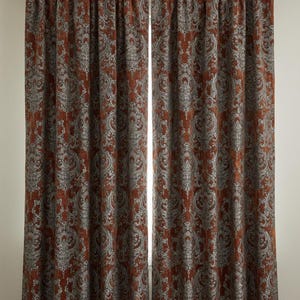 Op de afbeelding: Twee roestkleurige gordijnpanelen met een gedetailleerd, sierlijk damastpatroon in grijstinten en gebroken wit. De gordijnen hangen aan een metalen roede, wat zorgt voor een decoratieve en elegante raambekleding voor een woon- of slaapkamer.