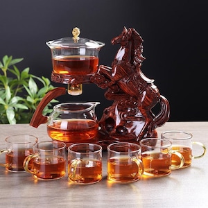 Könnte beinhalten: Ein Teeservice mit einer Holzpferdskulptur. Das Set enthält eine Glaskanne, einen Glasinfuser und sechs kleine Gläser mit goldenen Griffen. Der Tee hat eine bernsteinfarbene Farbe.