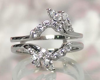 Puede incluir: Un protector de anillo plateado con un diseño floral. El anillo presenta piedras preciosas transparentes con tallas marquesa y redondas. Las piedras están engastadas en un delicado patrón en forma de hoja. El protector está diseñado para usarse con otro anillo.