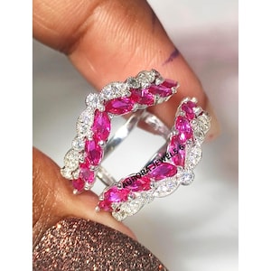 May include: A silver ring with a double band design. The ring is adorned with pink marquise-cut gemstones and small white round-cut gemstones. The text "AURORA JEWELS 6" is visible on the ring.