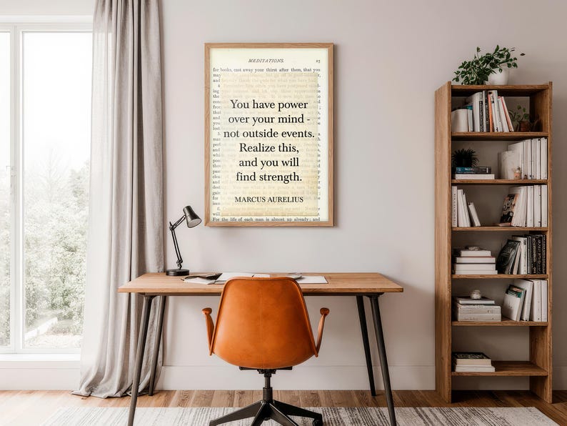 Puede incluir: Un cuadro enmarcado con la cita "Tienes poder sobre tu mente, no sobre los acontecimientos externos. Date cuenta de esto y encontrar&aacute;s la fuerza" de Marco Aurelio. El cuadro cuelga sobre un escritorio de madera con una l&aacute;mpara negra y una silla naranja.