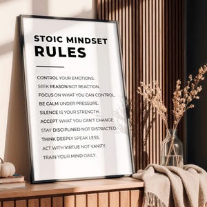 Może przedstawiać: Oprawiony wydruk z tekstem "STOIC MINDSET RULES" i listą zasad. Mała dynia i książki leżą na drewnianej powierzchni przed wydrukiem. Po prawej stronie wazon z suszonymi kwiatami. Wydruk znajduje się w pokoju.