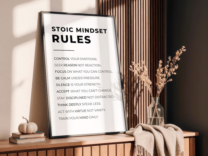 Może przedstawiać: Oprawiony wydruk z tekstem "STOIC MINDSET RULES" i listą zasad. Mała dynia i książki leżą na drewnianej powierzchni przed wydrukiem. Po prawej stronie wazon z suszonymi kwiatami. Wydruk znajduje się w pokoju.