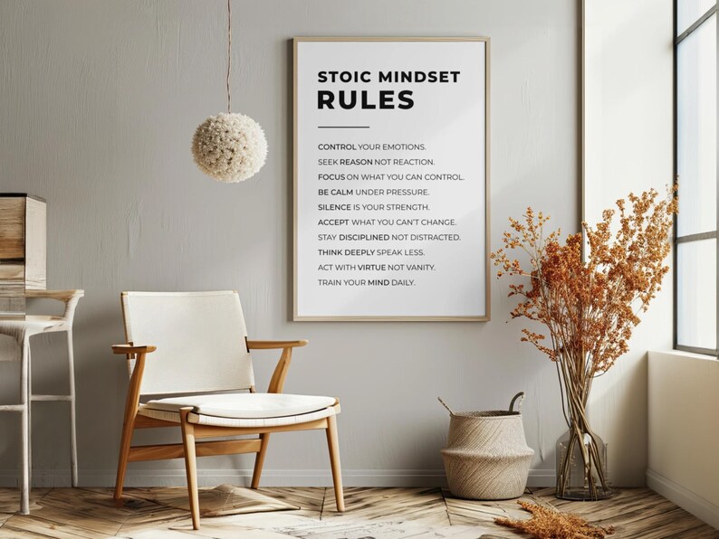 Może przedstawiać: Oprawiony wydruk z napisem "STOIC MINDSET RULES" wisi na szarej ścianie. Obok znajduje się drewniane krzesło z białym siedziskiem. Widoczna jest r&oacute;wnież dekoracyjna lampa wisząca i wazon z suszonymi roślinami.