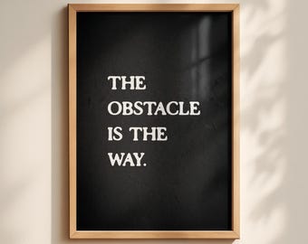 May include: A framed wall art piece featuring a black background with the white text THE OBSTACLE IS THE WAY. The print is enclosed in a light-colored wooden frame with a clean, rectangular design and a smooth, matte finish.