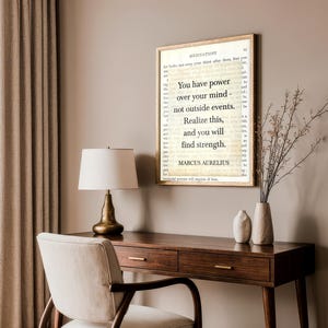 Puede incluir: Impresi&oacute;n enmarcada con la cita "Tienes poder sobre tu mente, no sobre los acontecimientos externos. Date cuenta de esto y encontrar&aacute;s la fuerza" de Marco Aurelio. Sobre un escritorio de madera con l&aacute;mpara y silla.