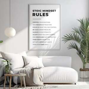 Może przedstawiać: Oprawiony wydruk z napisem "STOIC MINDSET RULES" wisi nad białą sofą. Na wydruku wymieniono zasady stoickiego nastawienia. Okrągła, biała lampa wisi u sufitu. Roślina doniczkowa znajduje się po lewej stronie sofy.