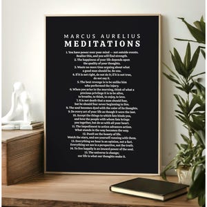 May include: A framed black and white print featuring the text "MARCUS AURELIUS MEDITATIONS." The print displays a list of philosophical quotes. The frame is a dark wood color, and the print is displayed on a wooden surface.