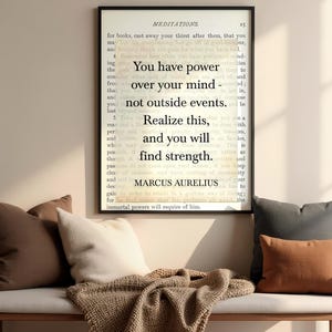 Puede incluir: Un cuadro enmarcado con la cita de Marco Aurelio: "Tienes poder sobre tu mente, no sobre los acontecimientos externos. Date cuenta de esto y encontrar&aacute;s la fuerza". Sobre un banco con cojines y una manta.