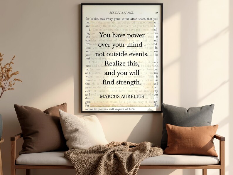 Puede incluir: Un cuadro enmarcado con la cita de Marco Aurelio: "Tienes poder sobre tu mente, no sobre los acontecimientos externos. Date cuenta de esto y encontrar&aacute;s la fuerza". Sobre un banco con cojines y una manta.
