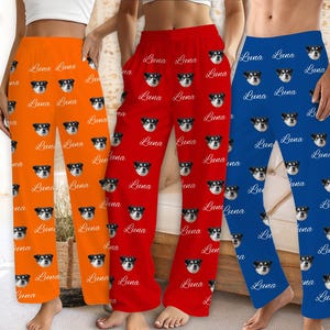 May include: Three pairs of pajama pants in orange, red, and blue. Each pair features a repeating pattern of a dog's face and the name "Luna" in a cursive font. The pants are loose-fitting and made of a soft material.