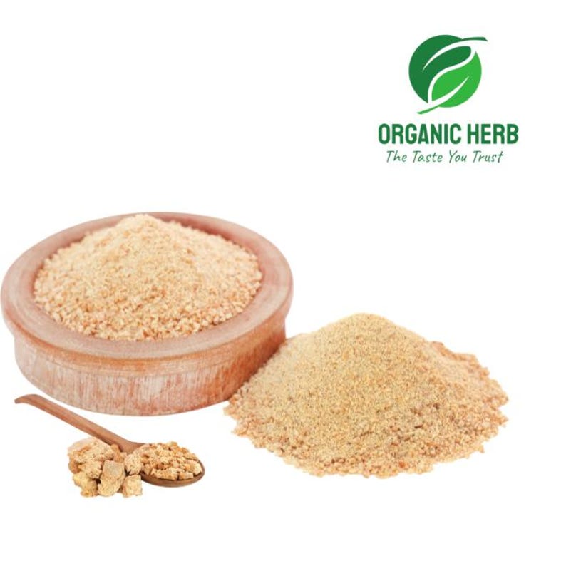 May include: A wooden bowl filled with light brown powder, a pile of the same powder, and a wooden spoon with a small amount of the powder and some chunks. The image also includes the text "ORGANIC HERB The Taste You Trust".
